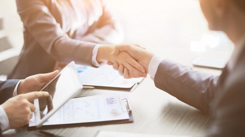 Two people shaking hands over a table.